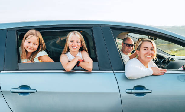 istock Happy young couple with two daughters inside car during auto trop. They are looking out auto windows, smiling, laughing during road trip. Family values, traveling concept side car view photo. 1780646689