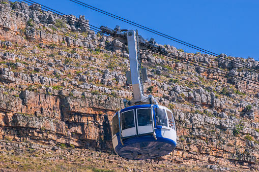 A cable car is seen ascending to Table Mountain National Park in Cape Town, South Africa.  It is a trip that almost all tourists make, to view the city from the top of the mountain. Photo shot in the afternoon sunlight on a clear, cloudless day; horizontal format. No people. Copy space.
