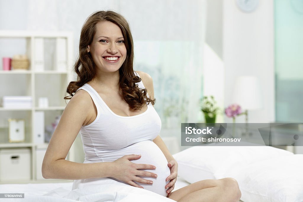 Pregnancy Photo of pretty pregnant woman keeping her hands on belly while looking at camera Abdomen Stock Photo