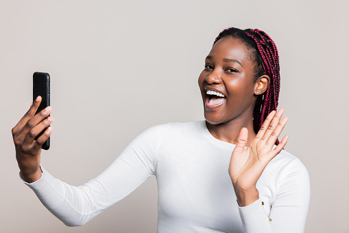 Delighted African Amerian dark skinned woman having video conference call holding cellphone in hands posing while shooting process.