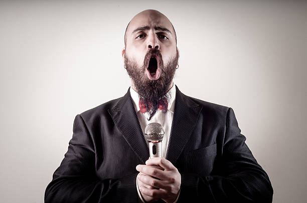 Bearded man singing on a microphone over a gray background stock photo