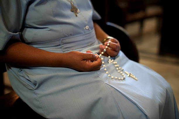 A Catholic woman holding beads in church People and religion, catholic sister praying in church and holding cross in hands. With model release nun praying cross human hand stock pictures, royalty-free photos & images