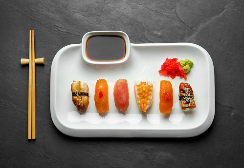 Plate with delicious nigiri sushi and soy sauce on black table, top view