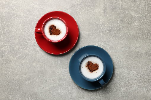 Cups of aromatic coffee with heart shaped decoration on light grey table, flat lay