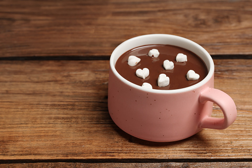 Cup of hot chocolate with heart shaped marshmallows on wooden table, space for text