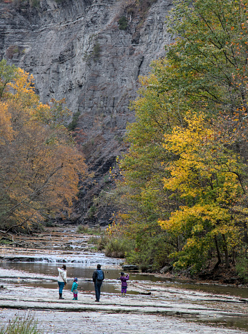 family walking inside gorge at  Taughannock Falls State Park, a tourist destination in the Finger Lakes region of upstate New York.  Famous waterfall in autumn with leaves changing color, foliage.