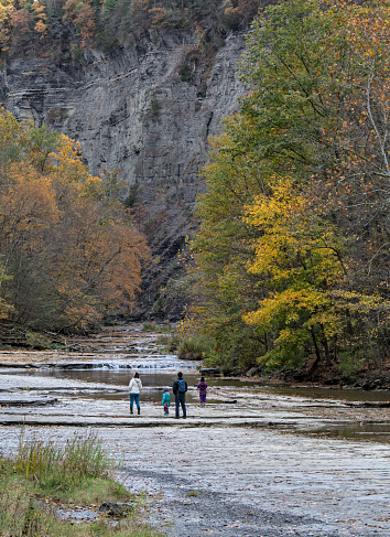family walking inside gorge at  Taughannock Falls State Park, a tourist destination in the Finger Lakes region of upstate New York.  Famous waterfall in autumn with leaves changing color, foliage.