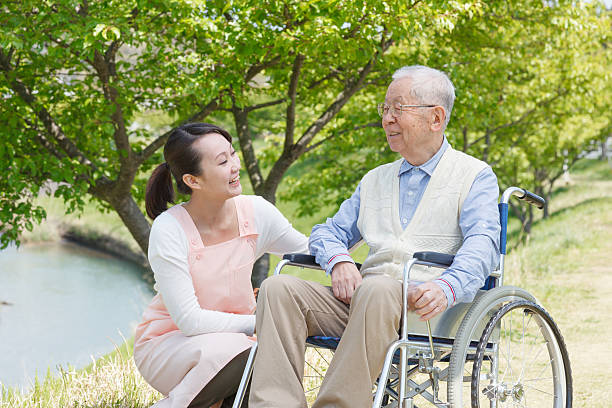 Senior man sitting on a wheelchair with caregiver stock photo