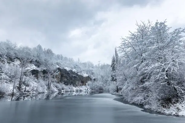 Photo of Winter snowy landscape with a lake by rock wall.