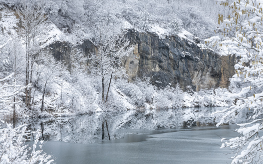 Winter snowy landscape with a lake by a rock wall.