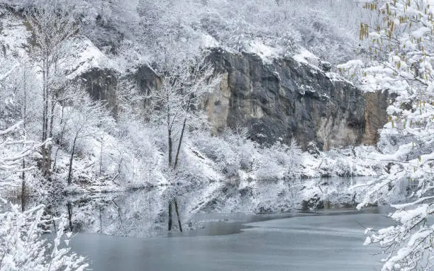 Photo of Winter snowy landscape with a lake by rock wall.