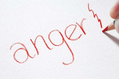 A red pencil hits a piece of paper with the word 'anger' written on it.