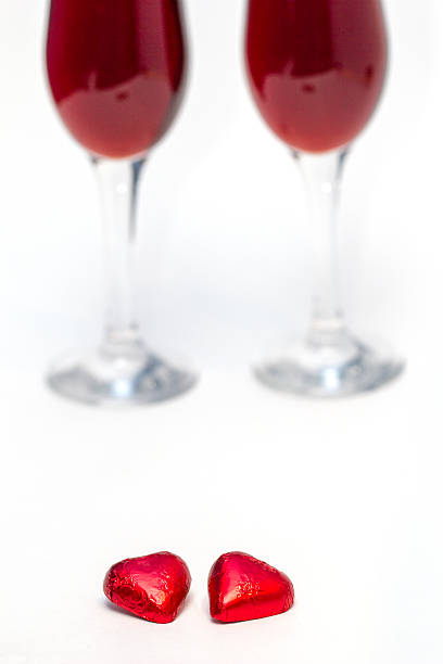 Heart shaped candies and two glasses of red wine on a white background