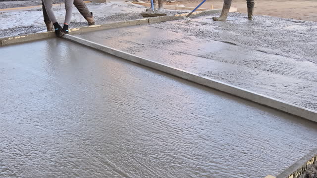 The concrete for driveway is being leveled by workers on construction site using mix concrete trowels
