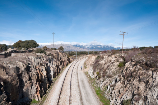 Cycling next to the railroad. At the background, snow capped peaks of the Guadarrama Mountains. Photo taken in Colmenar Viejo, Madrid Province, Spain