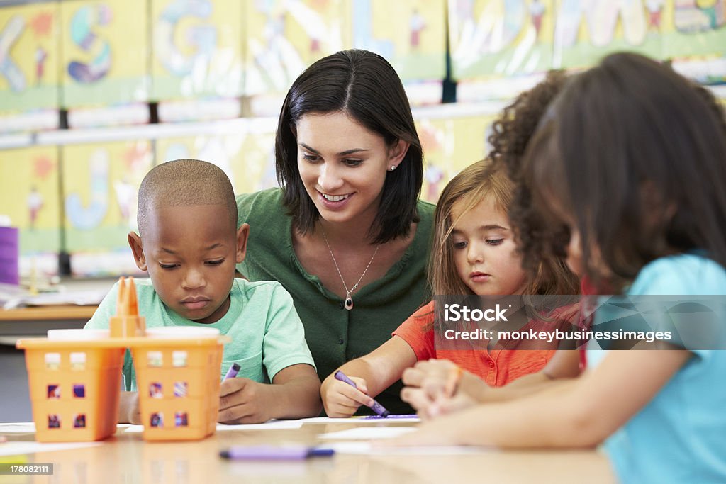 Elementary art class drawing with teacher at table Group Of Elementary Age Children In Art Class With Teacher Sitting Down At Table Drawing Teacher Stock Photo