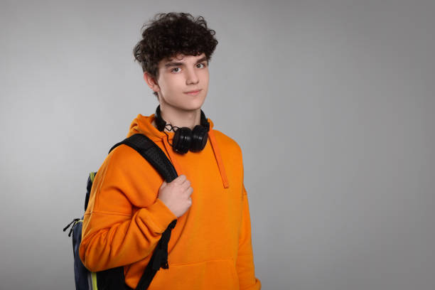 istock Teenage boy with headphones and backpack on light grey background. Space for text 1780823968