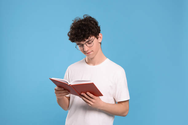 istock Teenage boy reading book on light blue background 1780827138