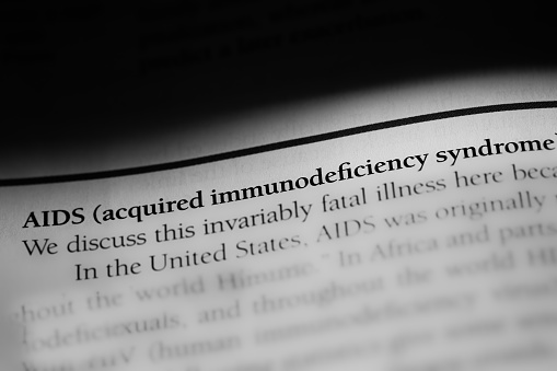 AIDS or acquired immunodeficiency syndrome, highly contagious autoimmune disease, printed in black on white page with selective focus and dramatic use of shadows.