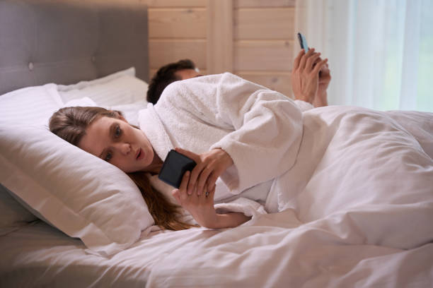 Surprised woman in bed with phone dressed in bathrobe