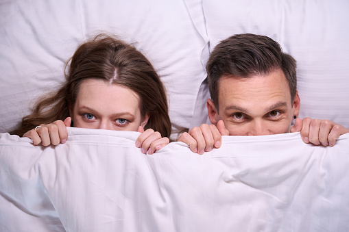 Close up of couple faces laying in bed and covered with white blanket