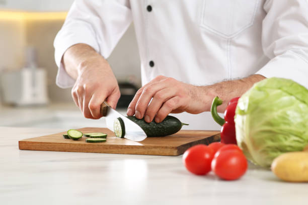 istock Chef cutting cucumber at marble table in kitchen, closeup 1780877303