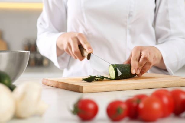 istock Professional chef cutting fresh cucumber at white table in kitchen, closeup 1780877306