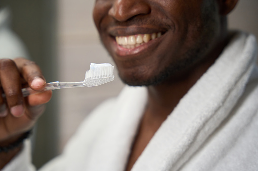 Man in a bathrobe is prepared to brush his teeth, he uses a toothbrush and toothpaste