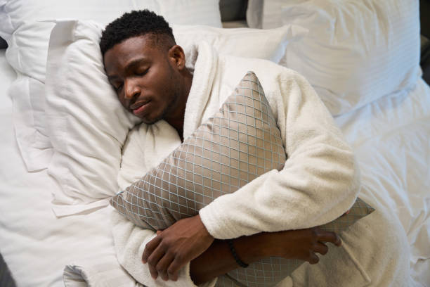 istock Curly-haired guy in terry robe sleeps sweetly on large bed 1780895822