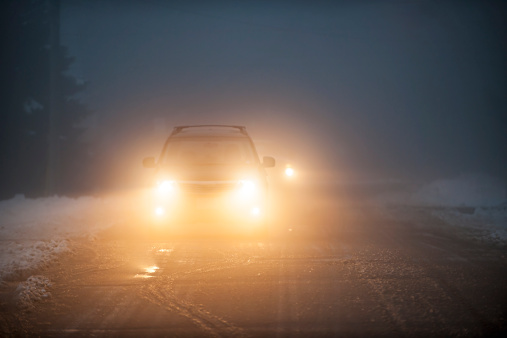 Bright headlights of a car driving on foggy winter road