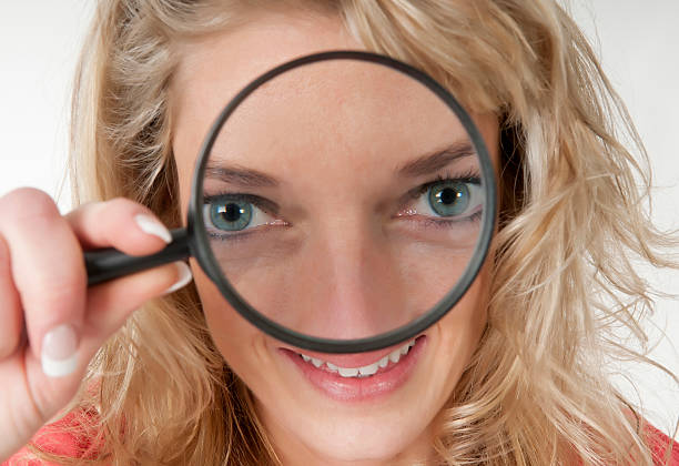 blond young woman with magnifying glass having two big eyes