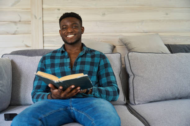 istock Young African American man sitting on the sofa with book 1780901494