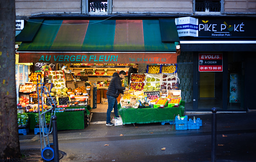Paris, France: A greengrocer stocking his colorful outdoor retail display on Rue des Martyrs in the 9th arrondissement.
