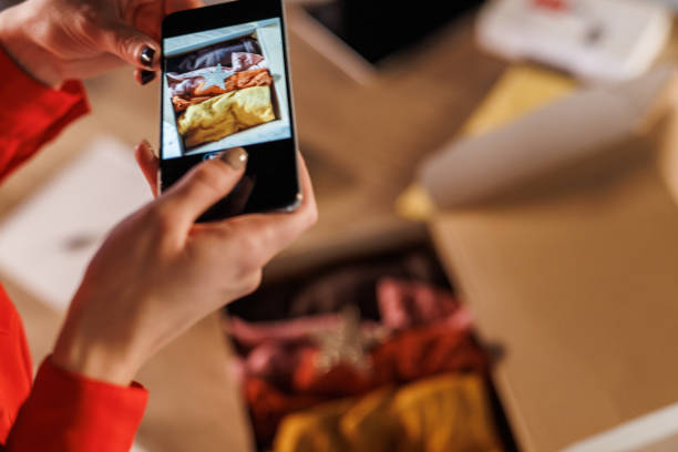 istock Young woman photographing clothes in a box that she packed for a customer supporting her small business 1780911648