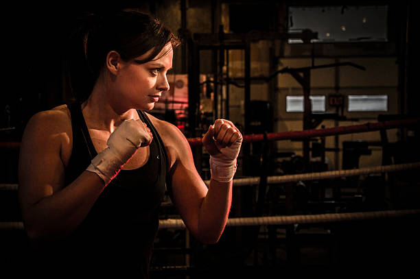 Girl Boxer in Fighting Stance Attractive female fighter holds hands in guard position, hand-wraps on her fists. fighting stance stock pictures, royalty-free photos & images