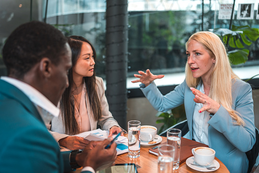 Embrace the fusion of diverse ideas and perspectives as a Black businessman, a Caucasian businesswoman, and an Asian businesswoman convene in a vibrant cafe, engaging in strategic planning for future growth and success.
