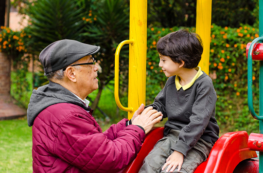 Senior man assisting playful grandson in sliding at playground