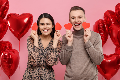 Lovely couple with decorative hearts near balloons on pink background