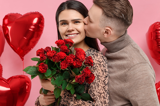 Happy couple celebrating Valentine's day, beloved woman with bouquet of red roses on pink background