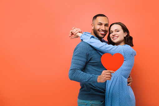 Lovely couple with paper heart on red background, space for text. Valentine's day celebration