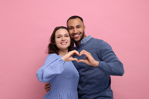 Lovely couple making heart with hands on pink background. Valentine's day celebration