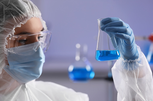 Scientist holding flask with light blue liquid in laboratory, closeup