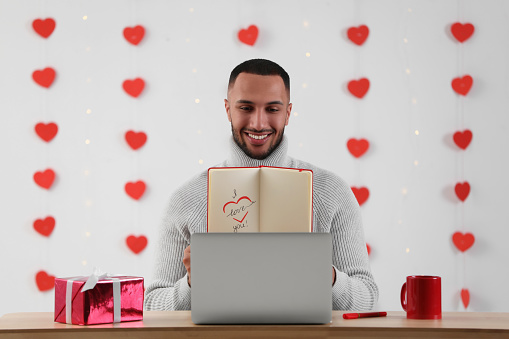 Valentine's day celebration in long distance relationship. Man having video chat with his girlfriend via laptop indoors