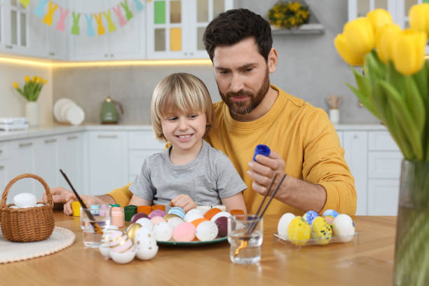 istock Father and his cute son painting Easter eggs at table in kitchen 1780966403
