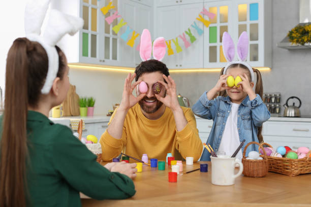 istock Father and daughter covering eyes with Easter eggs at table in kitchen. Family having fun 1780967013