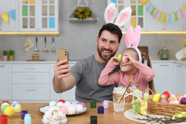 istock Father with his cute daughter making selfie at table in kitchen. Painting Easter eggs 1780967029
