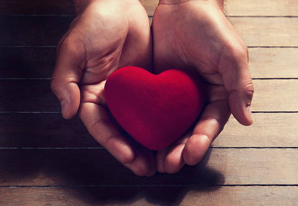 istock Hands cupping small red heart on wooden table  178099236