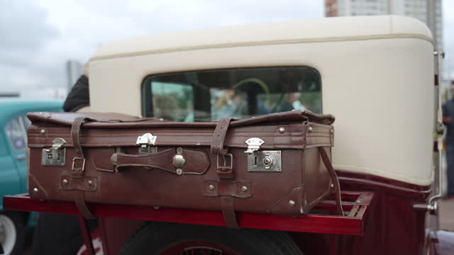 Old brown leather retro suitcase is fixed on open body of retro car.