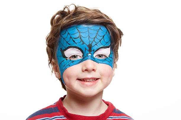 Child animator, artist's hand draws face painting to redhead child. Redhead boy with funny face painting. Painter makes reptile eyes at him. Children holiday, event, bithday party, entertainment.