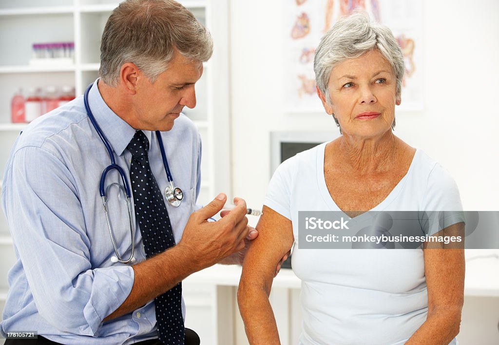 A senior male doctor injecting a senior female patient Doctor with female patient giving injection in surgery room Adult Stock Photo